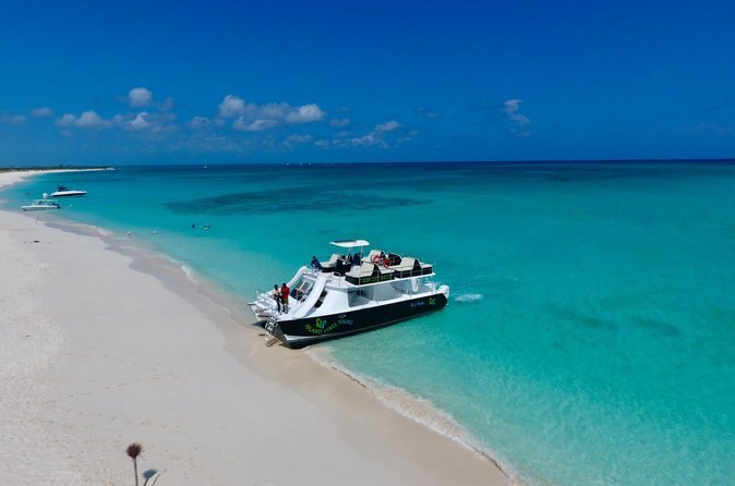 A boat pulled up at the tip of a white sandbar in clear water