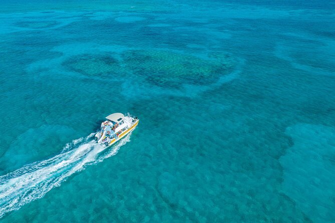 A boat crossing turquoise water dotted with dark reef patches, seen from above