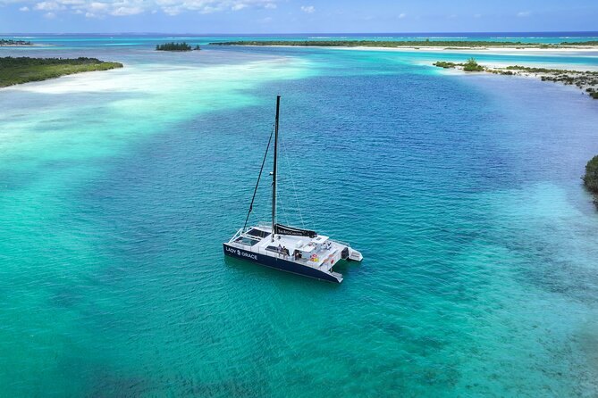 A sailing catamaran anchored in a turquoise lagoon between low green cays, seen from above
