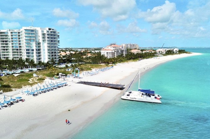 A catamaran anchored off a long white beach lined with resort buildings