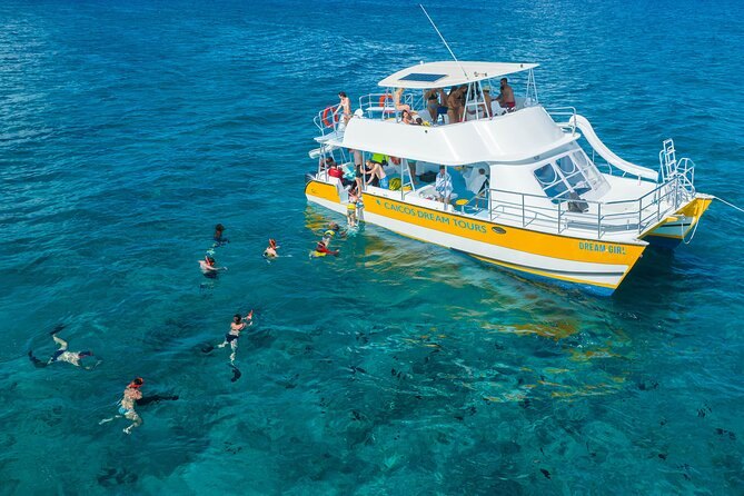 A double-decker catamaran at anchor with snorkelers in the water beside it