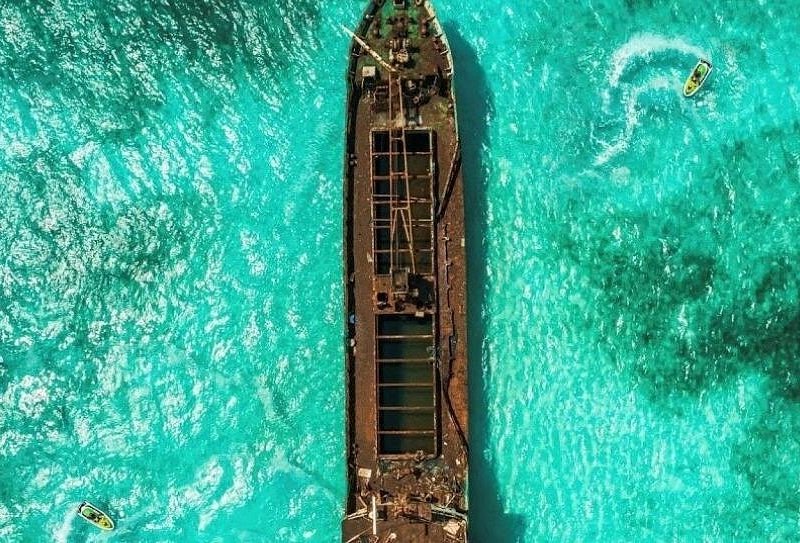 A rusting shipwreck lying in turquoise water, seen from directly above